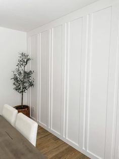 a dining room table with white chairs and a potted plant on the wall next to it