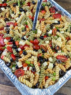 a pasta salad with olives, tomatoes and green peppers in a silver serving dish