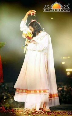 the woman is dressed in white and has flowers on her head as she stands next to an audience