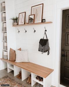 a wooden bench sitting in front of a white wall with hooks on it's sides