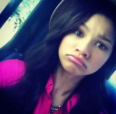 a woman with long black hair wearing a pink shirt and hat looking at the camera