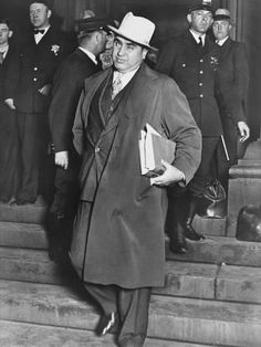 an old photo of a man in a suit and hat standing on steps with other men