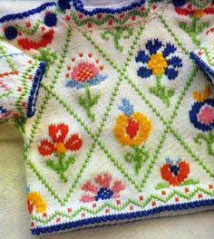 a white sweater with colorful flowers and blue trimmings on the front, sitting on top of a table