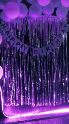 balloons and streamers are hanging from the ceiling in front of a purple backdrop that says happy birthday