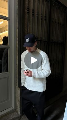 a man standing in front of a door looking at his cell phone while wearing a new york yankees hat