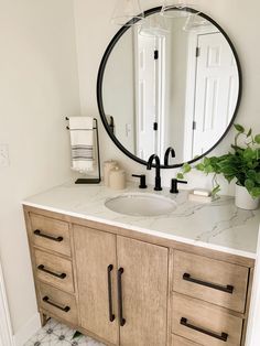 a bathroom vanity with a large round mirror above it and a potted plant on the counter