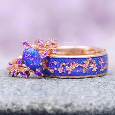 two wedding rings with purple and gold designs on them sitting on top of a rock