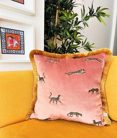 a yellow couch with a pink pillow on top of it next to a potted plant