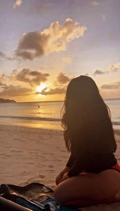 a woman sitting on top of a sandy beach next to the ocean