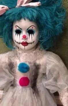 a creepy doll with blue hair and makeup on it's face, sitting against a wall