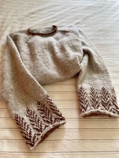 a sweater laying on top of a bed next to a white pillow with brown trim