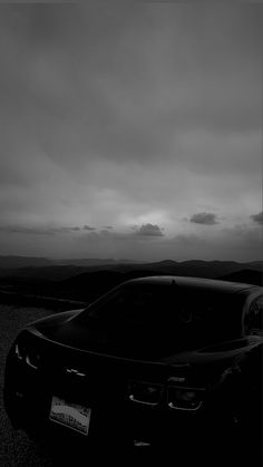 a black sports car parked on the side of a road with dark clouds in the background