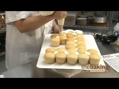 a baker is decorating cupcakes with icing on a white tray in the kitchen