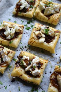 several square pieces of food with toppings sitting on top of a sheet of wax paper