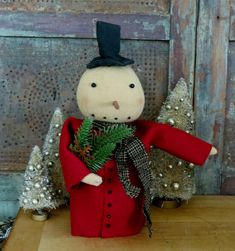 a doll with a red coat and black hat holding a fir tree in its hand