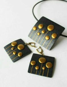 three black and gold square pendants on a white surface, one with four circles