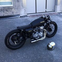 a black motorcycle parked in front of a garage door next to a helmet on the ground