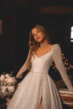 a woman in a white dress with long sleeves and a slited skirt is posing for the camera