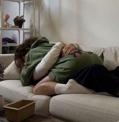 a woman laying on top of a white couch next to a wooden table and potted plant