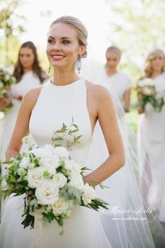 a bride standing in front of her bridals holding a bouquet and smiling at the camera