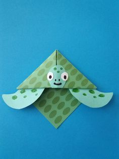 an origami turtle with green spots on it's body and eyes, sitting on a blue surface