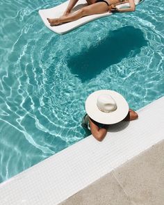 a woman in a white hat is floating on an inflatable raft next to a swimming pool