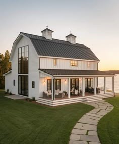 a white house with a black roof and two windows on the top floor is shown at sunset