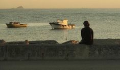 a man sitting on the edge of a wall looking out at boats in the water