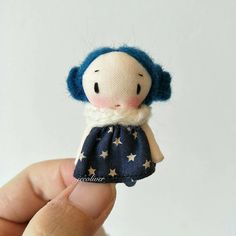 a hand holding a small doll with blue hair and stars on it's dress