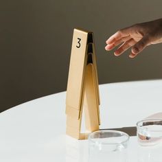 a person reaching for the number three in front of two glasses on a white table