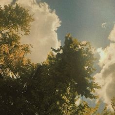 the sun shines through the clouds and trees in the foreground, as seen from below