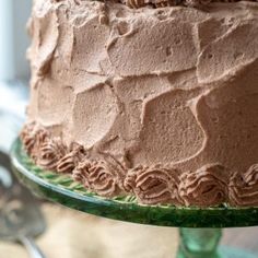 a chocolate cake sitting on top of a green glass platter covered in frosting