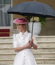 a woman in a white dress and pink hat holds an umbrella while standing on steps