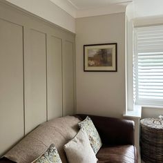 a brown leather couch sitting next to a window with shutters on the wall behind it