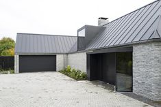 a modern house with black garage doors and brick driveway