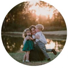 a mother and her two children hugging each other in front of a lake at sunset