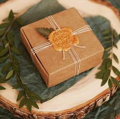 a brown gift box sitting on top of a wooden plate with greenery around it