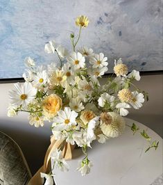 a bouquet of white and yellow flowers sitting on top of a table next to a chair