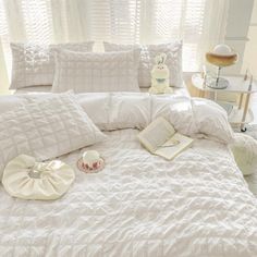 a bed with white comforters and pillows on top of it next to a window