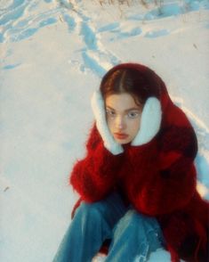 a woman sitting in the snow wearing a red and white fur coat over her head