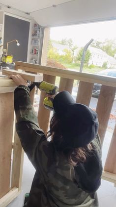 a woman in camouflage jacket painting wooden railing