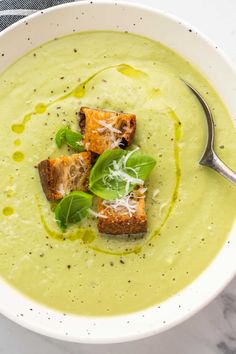 a white bowl filled with soup and topped with croutons, parmesan cheese and basil