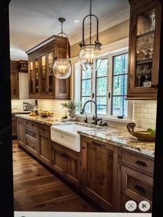 an image of a kitchen with wooden cabinets and marble counter tops, hanging lights over the sink