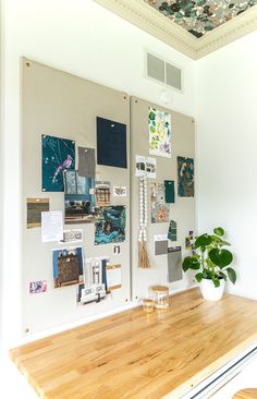 a wooden table topped with a potted plant next to a wall covered in pictures