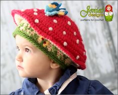 a young child wearing a crocheted strawberry hat