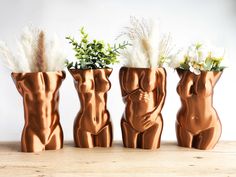 three vases with flowers and plants in them on a wooden table next to each other