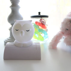 a white owl figurine sitting on top of a table next to a pink teddy bear