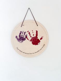 a wooden sign with two handprints on it hanging from a hook against a white wall