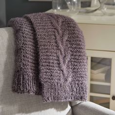 a knitted blanket sitting on top of a white couch next to a glass vase