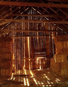 the inside of a barn with hay bales and sunlight coming through the windows on the ceiling